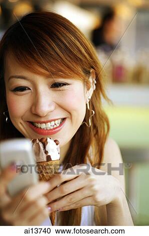 Young woman holding ice cream cone and mobile phone View Large Photo Image Stock Image - Young woman holding ice cream cone and mobile phone. Fotosearch