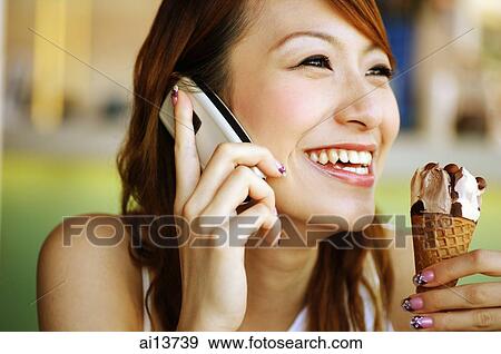 Young woman holding ice cream cone and using mobile phone View Large Photo Image Stock Photo - Young woman holding ice cream cone and using mobile phone. Fotosearch