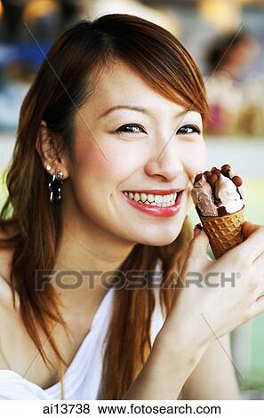 Stock Photo - Young woman holding ice cream cone, looking at camera. Fotosearch