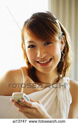 Young woman holding mobile phone, smiling at camera View Large Photo Image Stock Photo - Young woman holding mobile phone, smiling at camera. Fotosearch