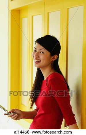 Young woman holding mobile phone, smiling at camera, sideview View Large Photo Image Stock Photo - Young woman holding mobile phone, smiling at camera, sideview. Fotosearch