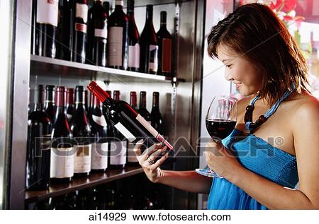Young woman holding wine glass, reading label on a bottle of wine View Large Photo Image Stock Photo - Young woman holding wine glass, reading label on a bottle of wine. Fotosearch