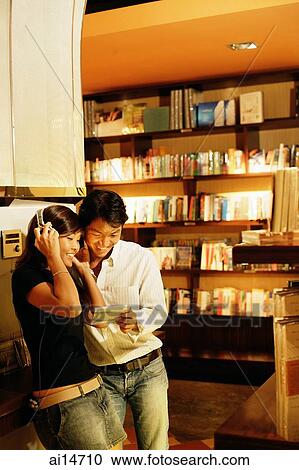 Stock Image - Young woman listening to CD, man standing next to her holding CD. Fotosearch