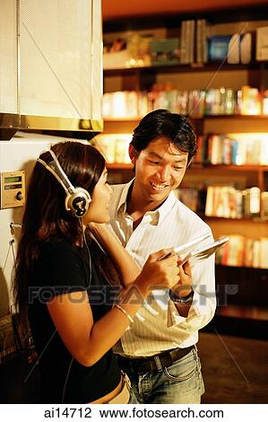 Young woman listening to CD, man standing next to her, looking at CD View Large Photo Image Stock Image - Young woman listening to CD, man standing next to her, looking at CD. Fotosearch
