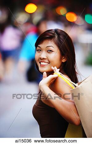 Young woman looking at camera, carrying shopping bag View Large Photo Image Stock Photograph - Young woman looking at camera, carrying shopping bag. Fotosearch