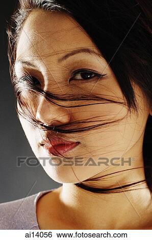 Young woman looking at camera, hair blown across her face View Large Photo Image Stock Photograph - Young woman looking at camera, hair blown across her face. Fotosearch