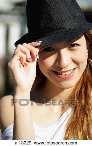 Stock Photo - Young woman looking at camera, wearing hat. Fotosearch