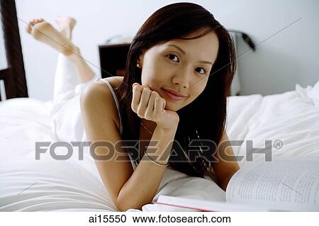 Young woman lying on bed, hand on chin, looking at camera View Large Photo Image Stock Image - Young woman lying on bed, hand on chin, looking at camera. Fotosearch
