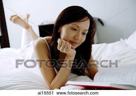 Young woman lying on bed, hand on chin, looking at book View Large Photo Image Stock Image - Young woman lying on bed, hand on chin, looking at book. Fotosearch