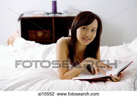 Young woman lying on bed, holding book, looking at camera View Large Photo Image Stock Image - Young woman lying on bed, holding book, looking at camera. Fotosearch