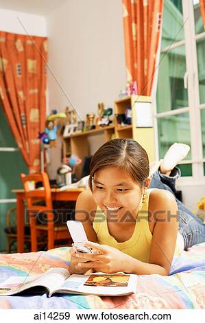 Stock Photo - Young woman, lying on bed holding mobile phone. Fotosearch