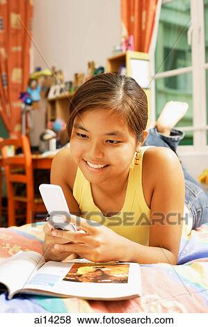 Stock Photo - Young woman, lying on bed looking at mobile phone. Fotosearch