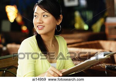 Young woman sitting at table, holding book, looking over shoulder View Large Photo Image Stock Photo - Young woman sitting at table, holding book, looking over shoulder. Fotosearch