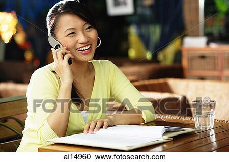 Young woman sitting at table, notebook open in front of her, using mobile phone View Large Photo Image Stock Image - Young woman sitting at table, notebook open in front of her, using mobile phone. Fotosearch