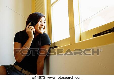Young woman sitting next to window, using mobile phone View Large Photo Image Stock Image - Young woman sitting next to window, using mobile phone. Fotosearch
