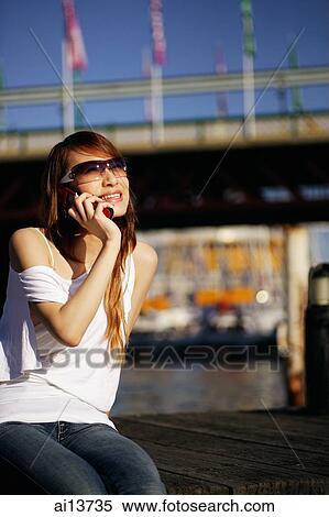 Young woman sitting on jetty, using mobile phone View Large Photo Image Stock Photography - Young woman sitting on jetty, using mobile phone. Fotosearch