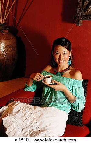 Young woman sitting on sofa, holding cup and saucer View Large Photo Image Stock Image - Young woman sitting on sofa, holding cup and saucer. Fotosearch