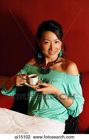 Young woman sitting on sofa, holding cup and saucer, portrait View Large Photo Image Stock Image - Young woman sitting on sofa, holding cup and saucer, portrait. Fotosearch