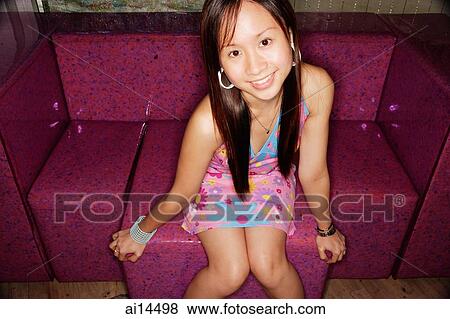 Young woman sitting on sofa, looking up at camera View Large Photo Image Stock Photo - Young woman sitting on sofa, looking up at camera. Fotosearch