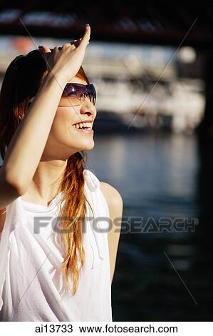 Young woman wearing sunglasses, shielding eyes, looking away View Large Photo Image Stock Image - Young woman wearing sunglasses, shielding eyes, looking away. Fotosearch