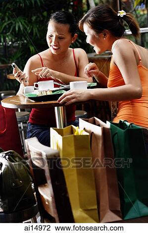 Young women at cafe, looking at mobile phone View Large Photo Image Stock Image - Young women at cafe, looking at mobile phone. Fotosearch