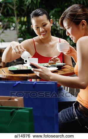 Young women at cafe, one looking at mobile phone View Large Photo Image Stock Photograph - Young women at cafe, one looking at mobile phone. Fotosearch