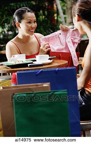 Young women at cafe, one showing items from shopping bag View Large Photo Image Stock Photography - Young women at cafe, one showing items from shopping bag. Fotosearch