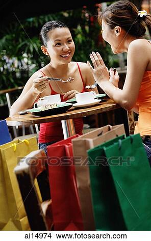 Picture - Young women at cafe, talking over coffee, shopping bags behind them. Fotosearch