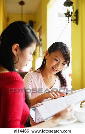 Young women in cafe, looking at newspaper together, sitting side by side View Large Photo Image Stock Photograph - Young women in cafe, looking at newspaper together, sitting side by side. Fotosearch