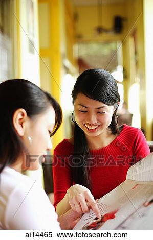 Stock Photography - Young women in cafe, looking at newspaper. Fotosearch