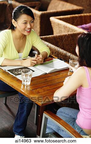 Young women sitting across each other at cafe, talking View Large Photo Image Stock Image - Young women sitting across each other at cafe, talking. Fotosearch