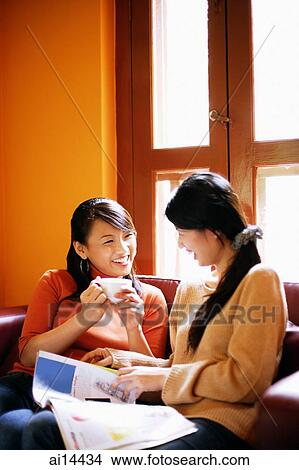 Young women sitting in living room, one holding cup, the other holding newspaper View Large Photo Image Picture - Young women sitting in living room, one holding cup, the other holding newspaper. Fotosearch