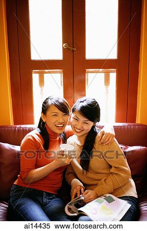 Young women sitting in living room, one holding cup, looking at camera View Large Photo Image Stock Photography - Young women sitting in living room, one holding cup, looking at camera. Fotosearch