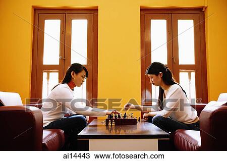 Young women sitting in living room, playing chess View Large Photo Image Stock Image - Young women sitting in living room, playing chess. Fotosearch
