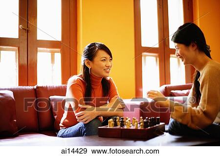 Young women sitting in living room, chess board on table between them View Large Photo Image Stock Photo - Young women sitting in living room, chess board on table between them. Fotosearch
