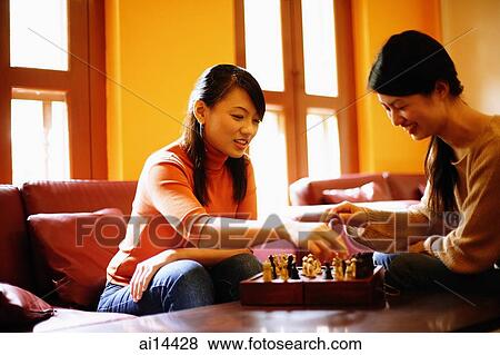 Young women sitting, playing chess in living room View Large Photo Image Stock Photo - Young women sitting, playing chess in living room. Fotosearch