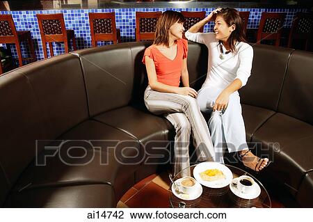 Young women sitting side by side, talking, food on table in front of them View Large Photo Image Stock Image - Young women sitting side by side, talking, food on table in front of them. Fotosearch