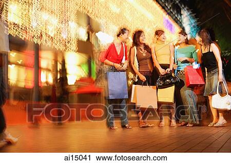 Stock Image - Young women standing side by side, carrying shopping bags. Fotosearch