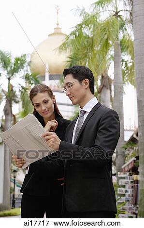 Businessman and businesswoman looking at newspaper, mosque in the background View Large Photo Image Stock Photo - Businessman and businesswoman looking at newspaper, mosque in the background . Fotosearch