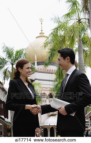 Businessman and businesswoman shaking hands, Mosque in the background View Large Photo Image Picture - Businessman and businesswoman shaking hands, Mosque in the background . Fotosearch