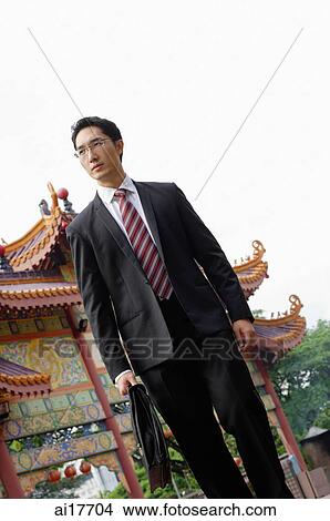 Businessman carrying briefcase, Chinese temple in the background View Large Photo Image Picture - Businessman carrying briefcase, Chinese temple in the background . Fotosearch