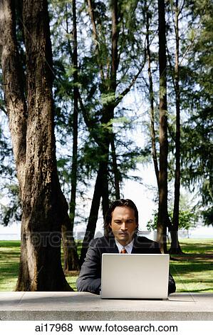 Stock Photo - Businessman in park, using laptop . Fotosearch