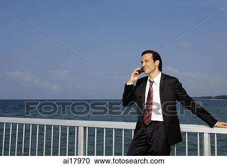 Businessman leaning on railing, using mobile phone View Large Photo Image Stock Image - Businessman leaning on railing, using mobile phone . Fotosearch
