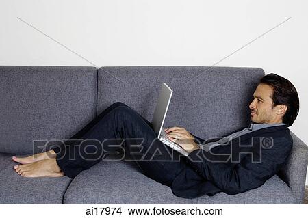 Businessman lying on sofa, using laptop View Large Photo Image Picture - Businessman lying on sofa, using laptop . Fotosearch