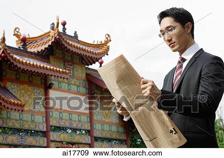 Businessman reading newspaper, Chinese temple in the background View Large Photo Image Stock Photo - Businessman reading newspaper, Chinese temple in the background. Fotosearch
