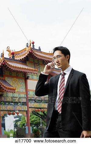 Businessman standing in front of Chinese temple, using mobile phone View Large Photo Image Stock Image - Businessman standing in front of Chinese temple, using mobile phone . Fotosearch