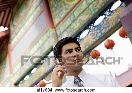 Picture - Businessman standing in front of temple gate, using mobile phone . Fotosearch