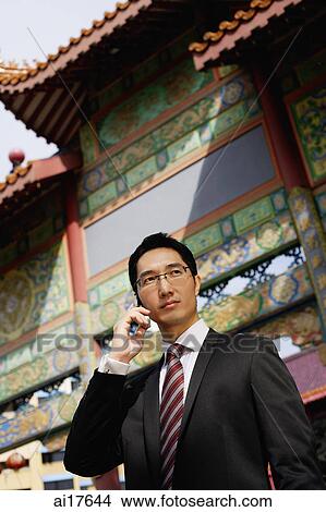 Businessman standing in front of temple gate, using mobile phone View Large Photo Image Picture - Businessman standing in front of temple gate, using mobile phone . Fotosearch