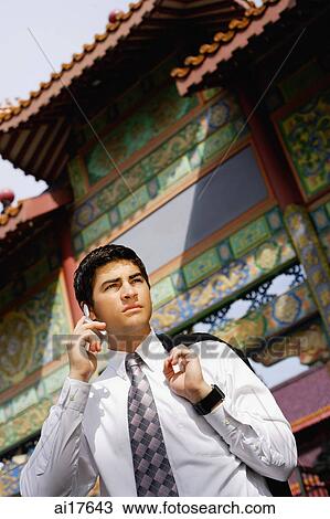 Businessman standing in front of temple gate, holding jacket over shoulder, using mobile phone View Large Photo Image Stock Image - Businessman standing in front of temple gate, holding jacket over shoulder, using mobile phone . Fotosearch