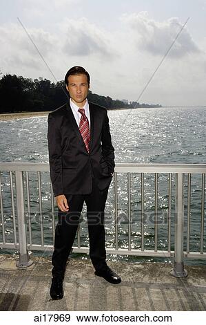 Businessman standing next to sea, hand in pocket, looking at camera View Large Photo Image Stock Photo - Businessman standing next to sea, hand in pocket, looking at camera . Fotosearch
